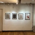 A collection of four framed drawings in black frames on against a white wall.